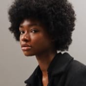 A young Black woman with an afro looks thoughtfully to the side